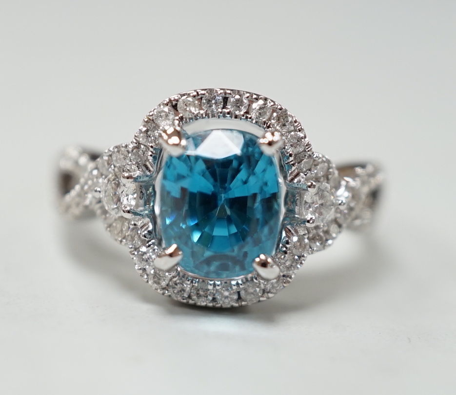 A modern 14k white metal, cushion cut blue zircon and diamond chip set cluster dress ring, with diamond chip set shoulders, size O, gross weight 6.8 grams.